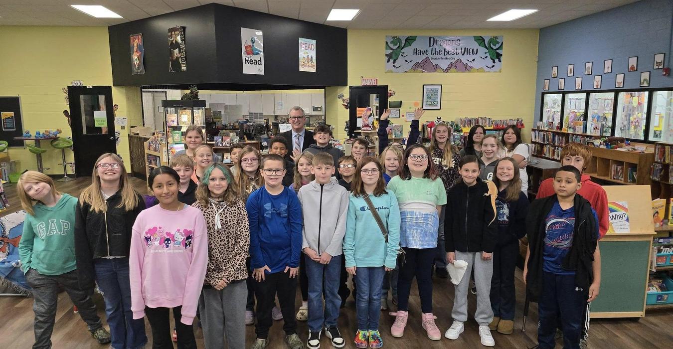 A group of smiling students poses together in a library with colorful decor.