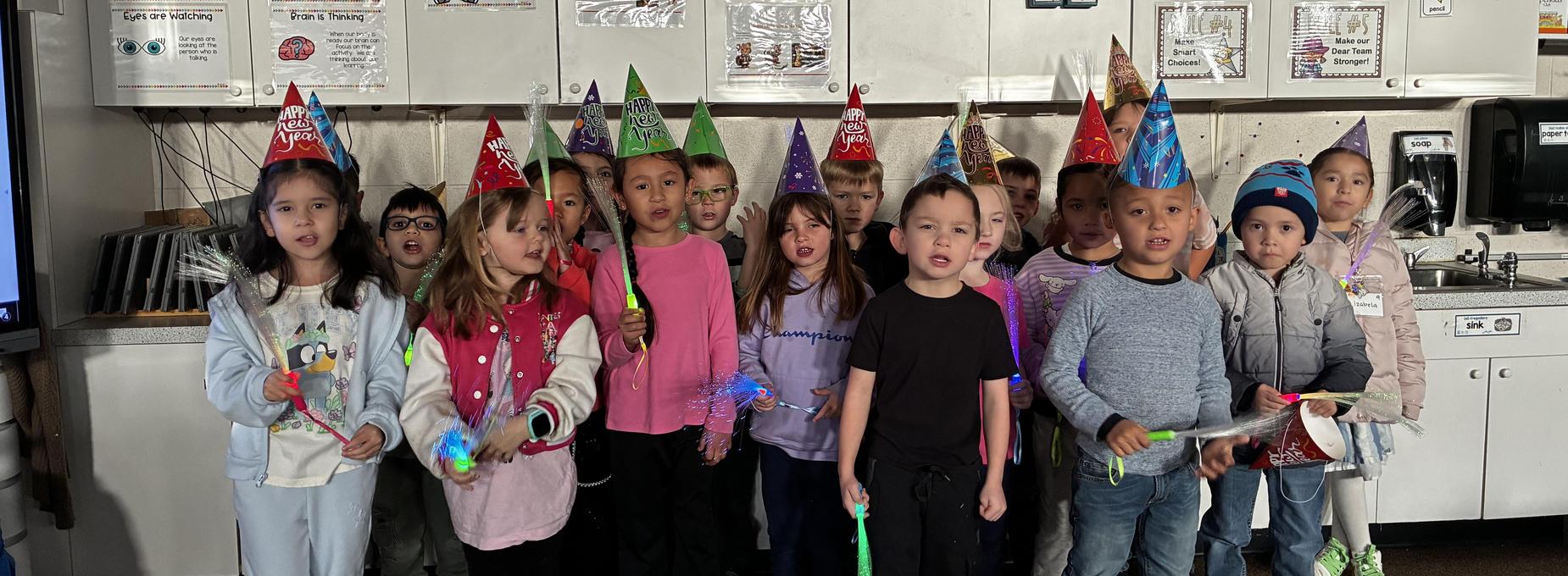 Group of children wearing party hats, singing with light toys in a classroom setting