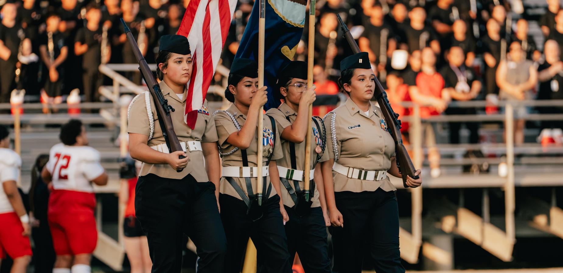 A color guard marching with flags in front of a large audience.