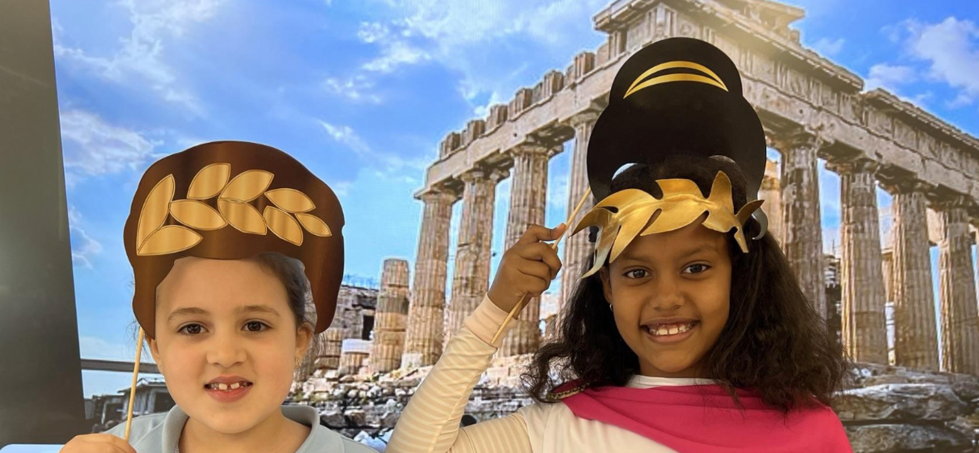 Two children wearing accessories against a backdrop of ancient ruins.