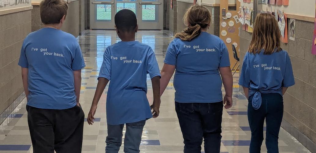 back of four students walking down the hall with "I've got your back" on their shirts