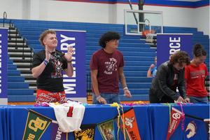 Students express excitement while signing letters at a celebration event with banners.