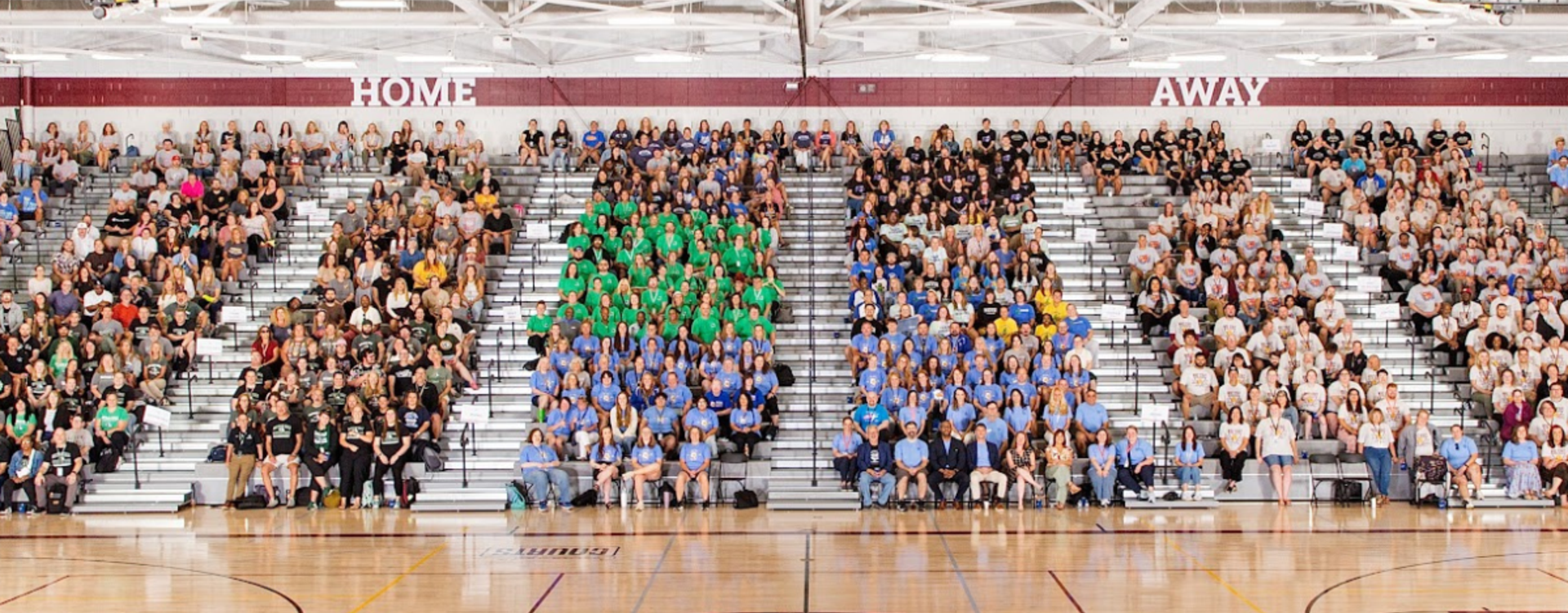 A large crowd of people in different colored shirts seated in a gymnasium.