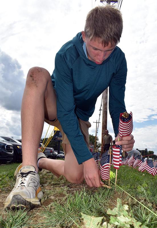 A young man setting up a flag with a grass-covered knee.