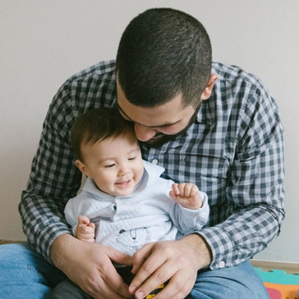 A father and baby sitting together, both smiling joyfully.
