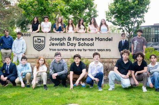 Students posing in front of a school sign surrounded by greenery.