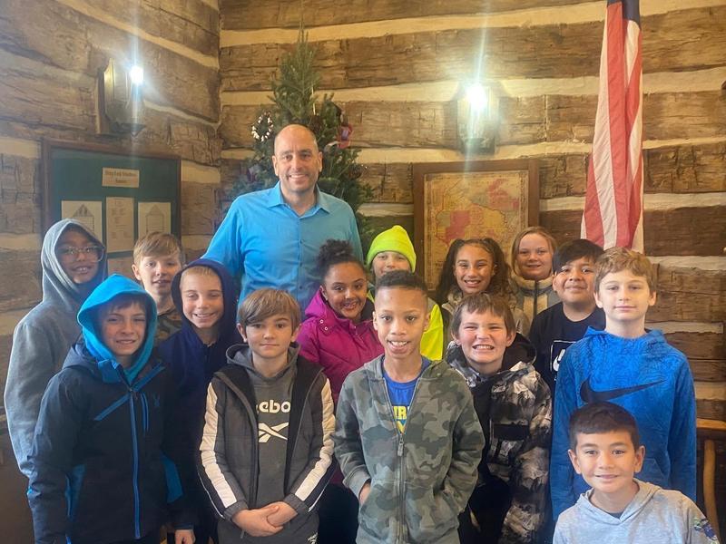 A group of children and an adult posing together in a rustic indoor setting.