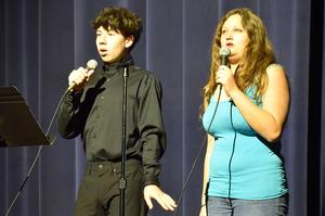 Young man and woman singing together with microphones on stage.