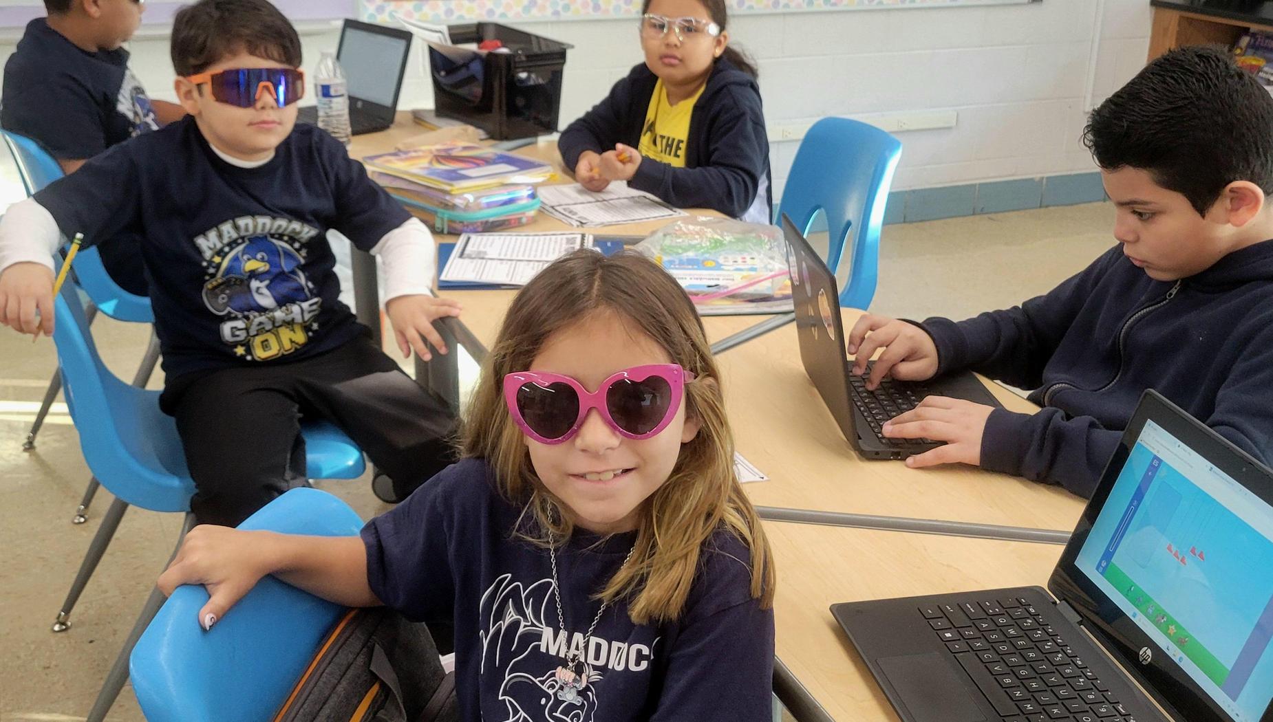 Students in a classroom engaged in various activities, wearing sunglasses and using laptops.