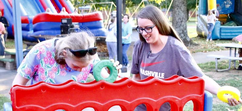 Student explores a ring-toss game with guidance from a staff member at an outdoor event.