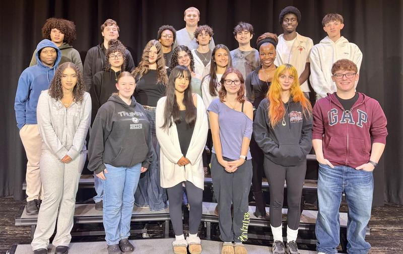 A group of high school students smiling on stage risers.