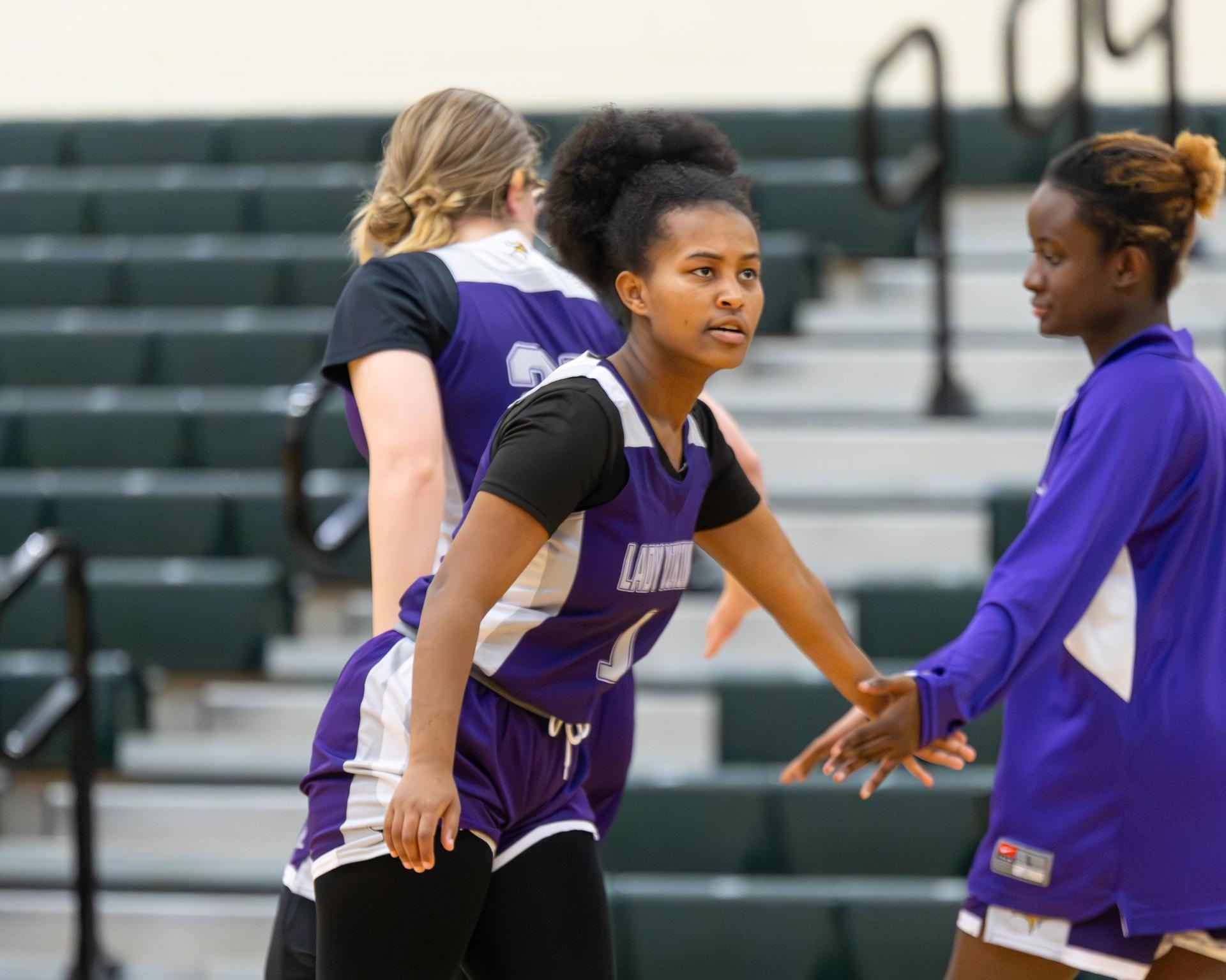 Two varsity girls basketball players slapping hands while warming up for a game.