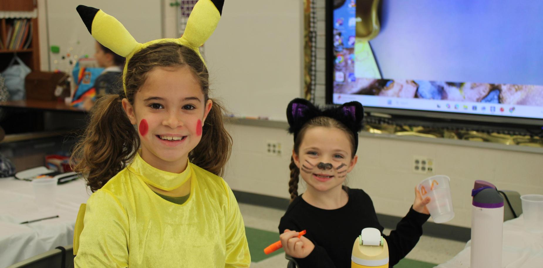 Two girls, one dressed as Pikachu and the other as a cat, smiling at the camera.