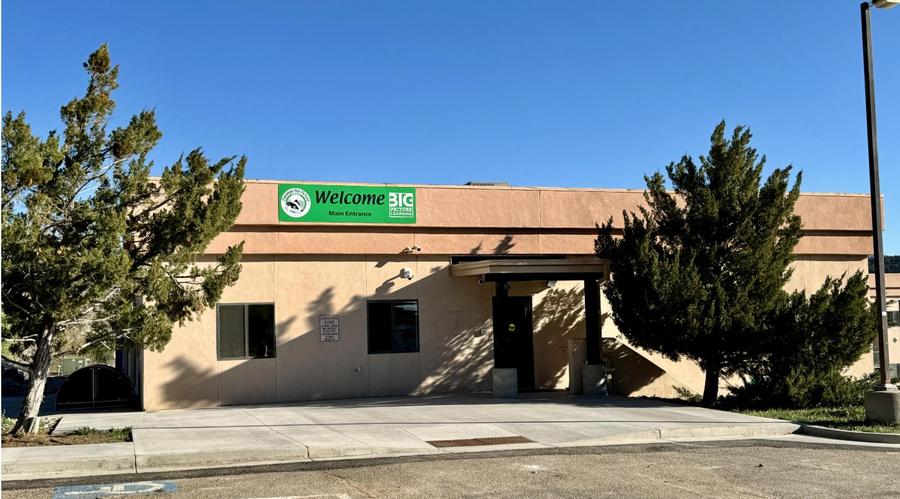 Single-story building with a green welcome sign and surrounding trees.