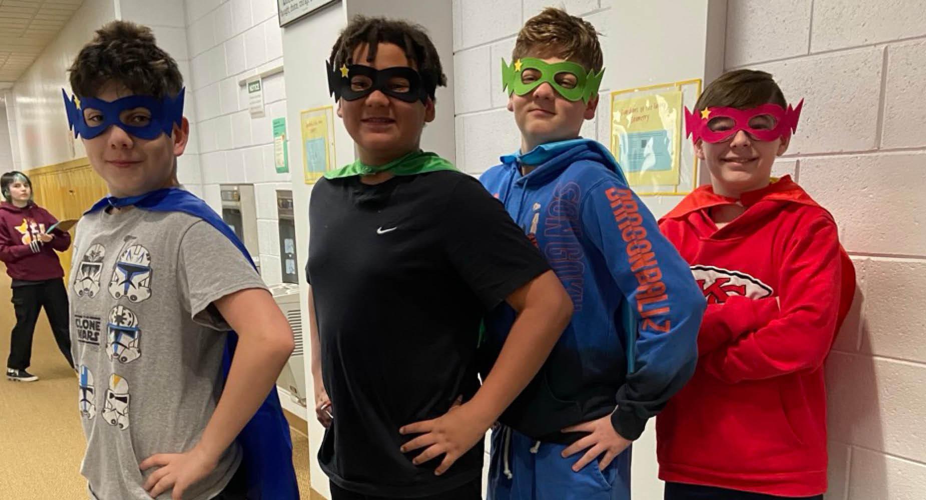 4 male students wear superhero masks and capes and stand with hands on hips