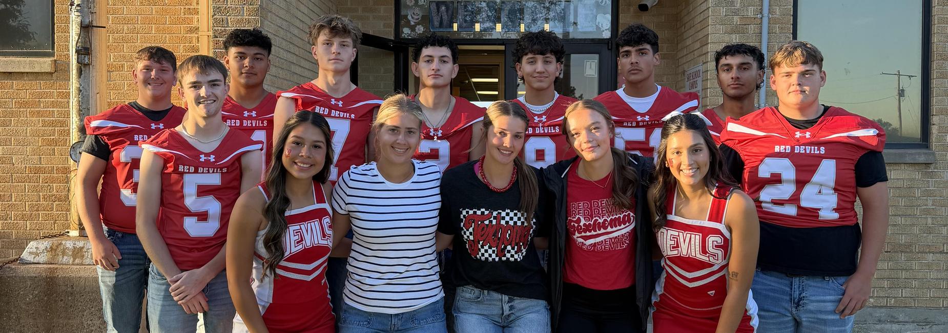 Group of cheerleaders and football players in red uniforms, posed together outdoors.