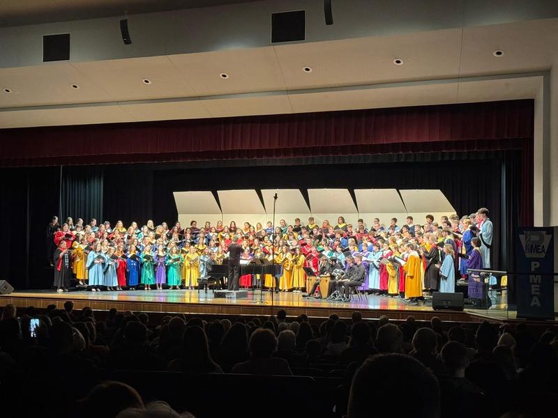 large choir on stage dressed in multi-colored choir robes