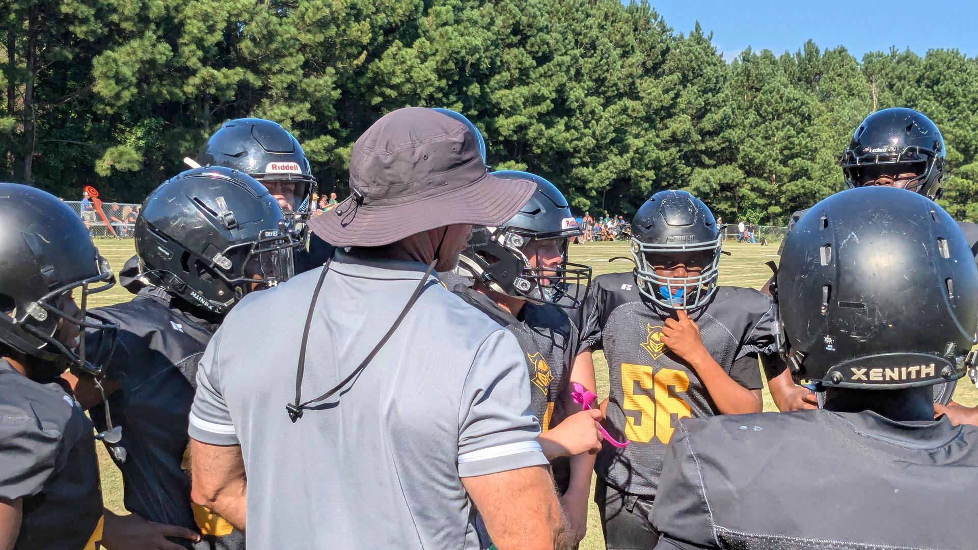 A youth football team huddles together while a coach gives instructions.