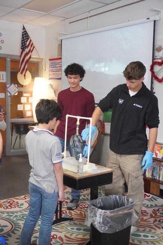 Two high school students show a pig lung as one 4th grader examines it.