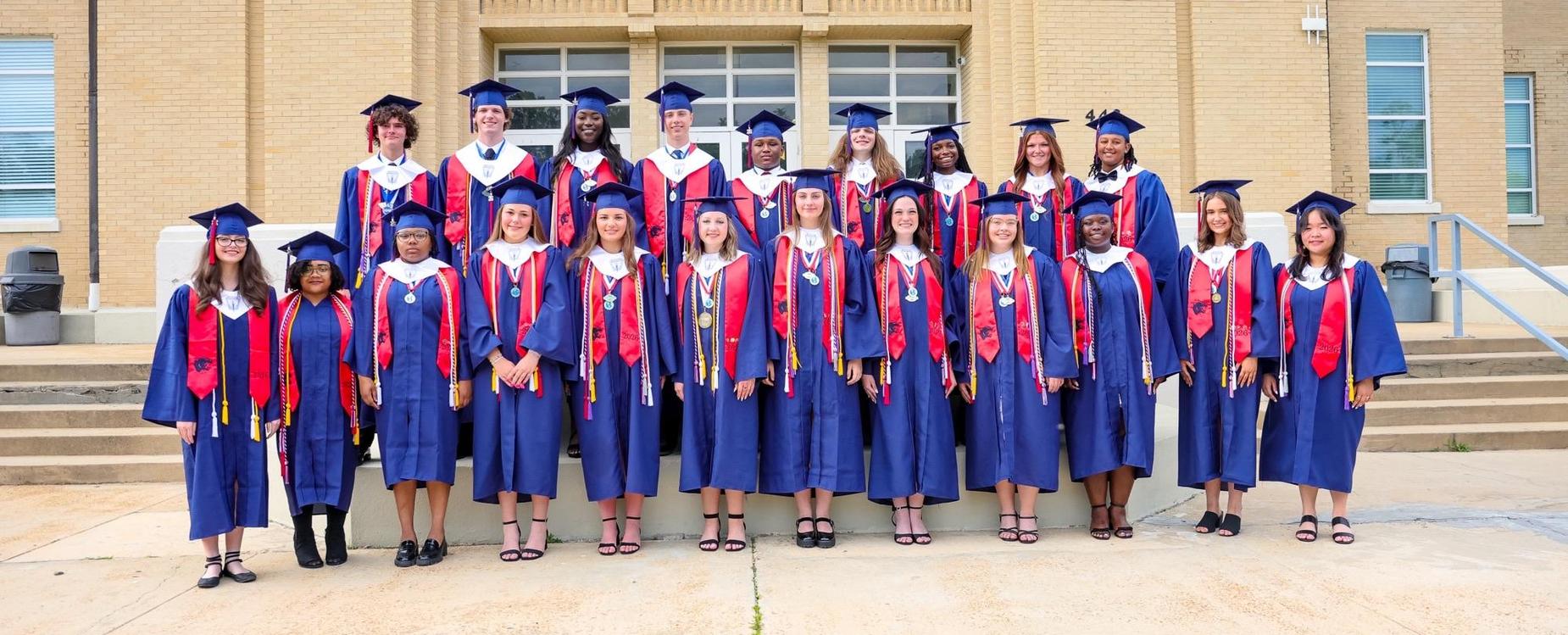 Group of graduates wearing caps and gowns outside a school building.