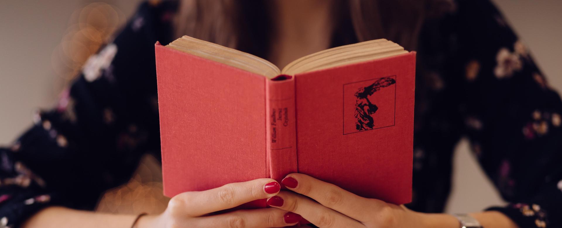 Person holding a red book with a floral background.