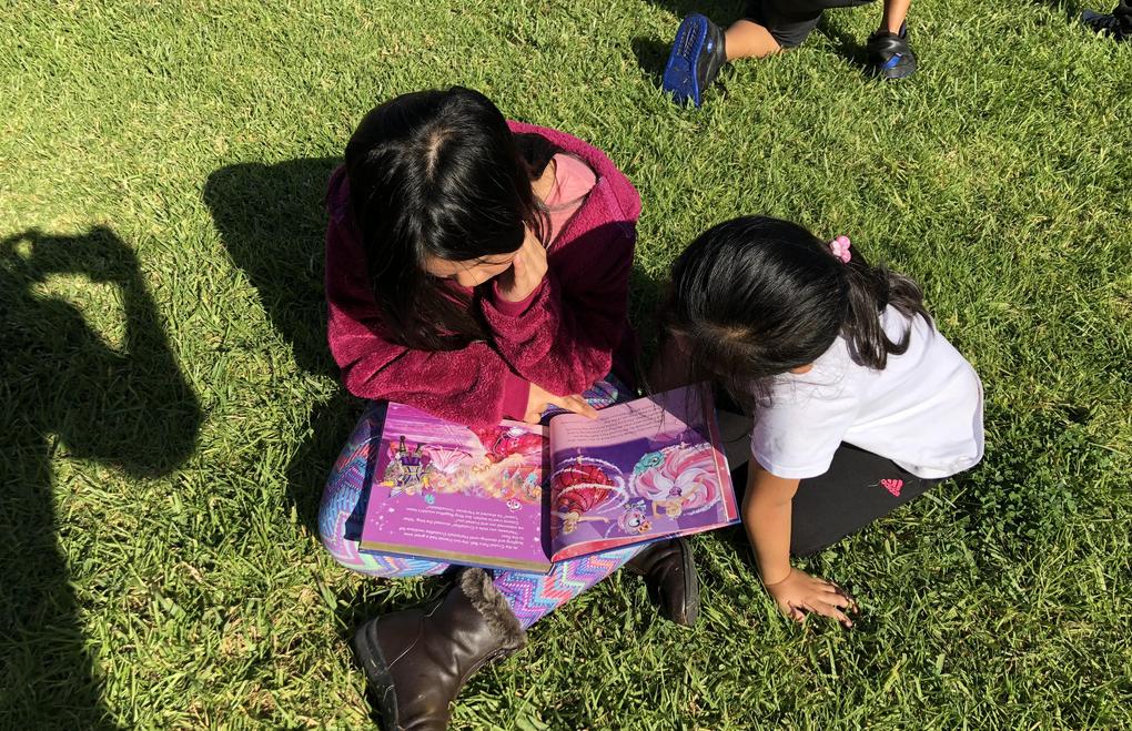 Two students sit together reading a book.