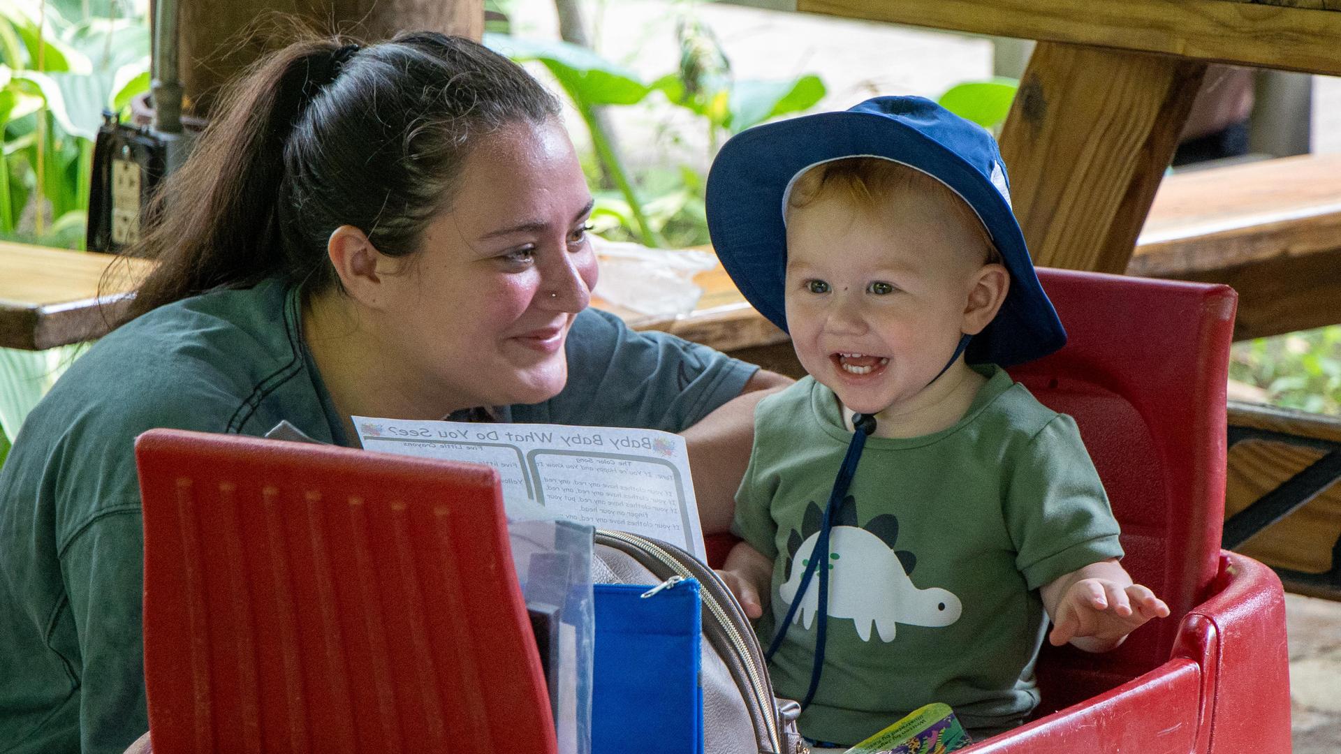 IU5 Elect student and their toddler in a blue hat sitting in a red wagon are smiling, enjoying the program's trip to the Erie Zoo.