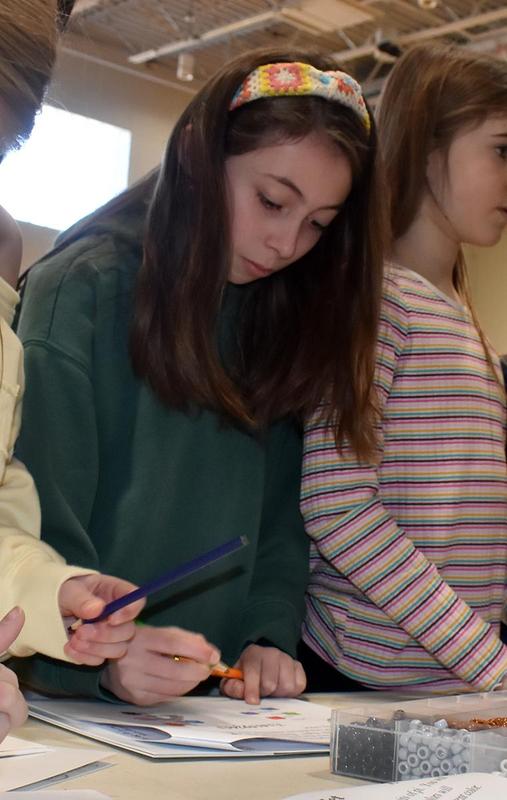 a girl drawing on a piece of paper with a crayon