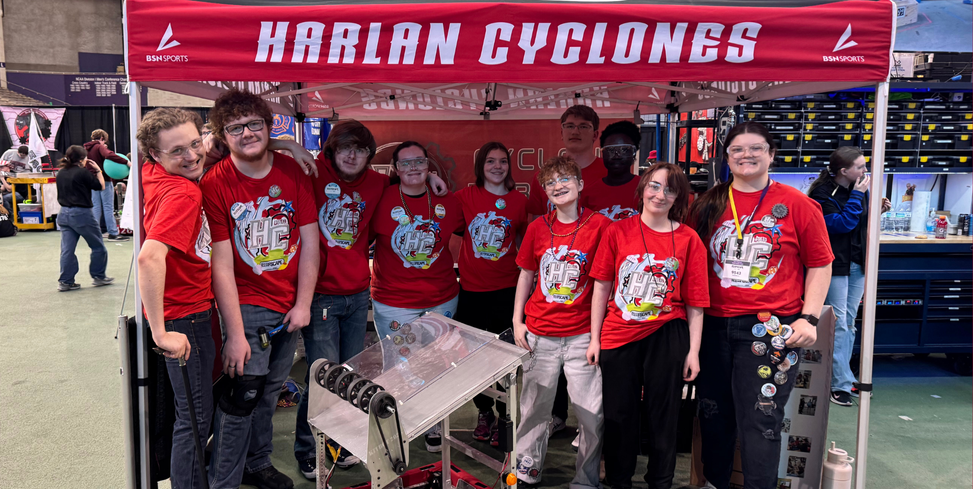A group of students wearing matching shirts stands under a team tent at an event.