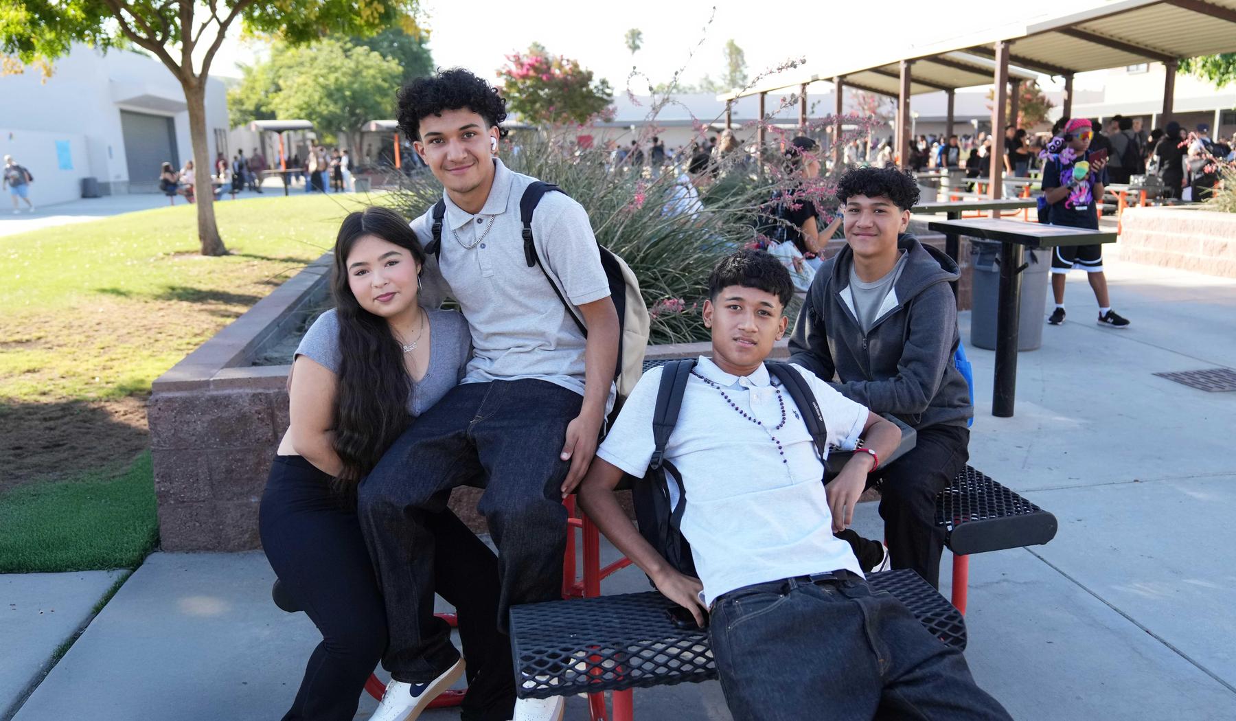 four high school students sitting at picnic table before school begins