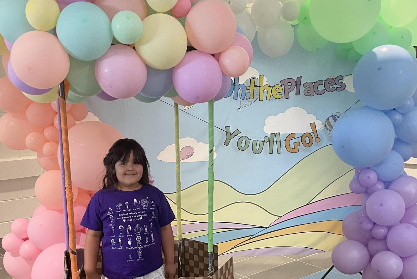 Child standing under a balloon arch with a hot air balloon backdrop.