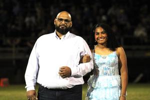 A man and a woman in formal attire walking together on a football field.