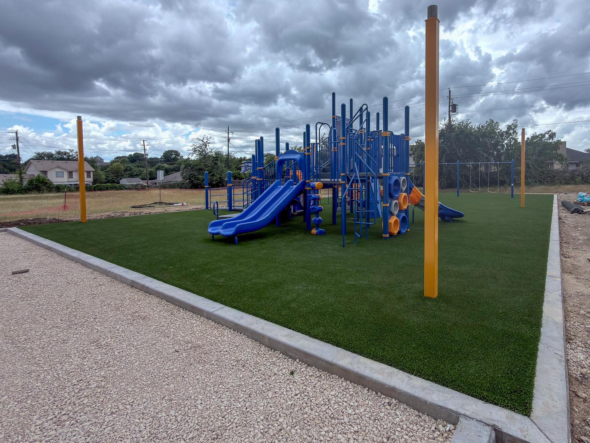 A completed playground featuring slides and climbing structures on green turf.