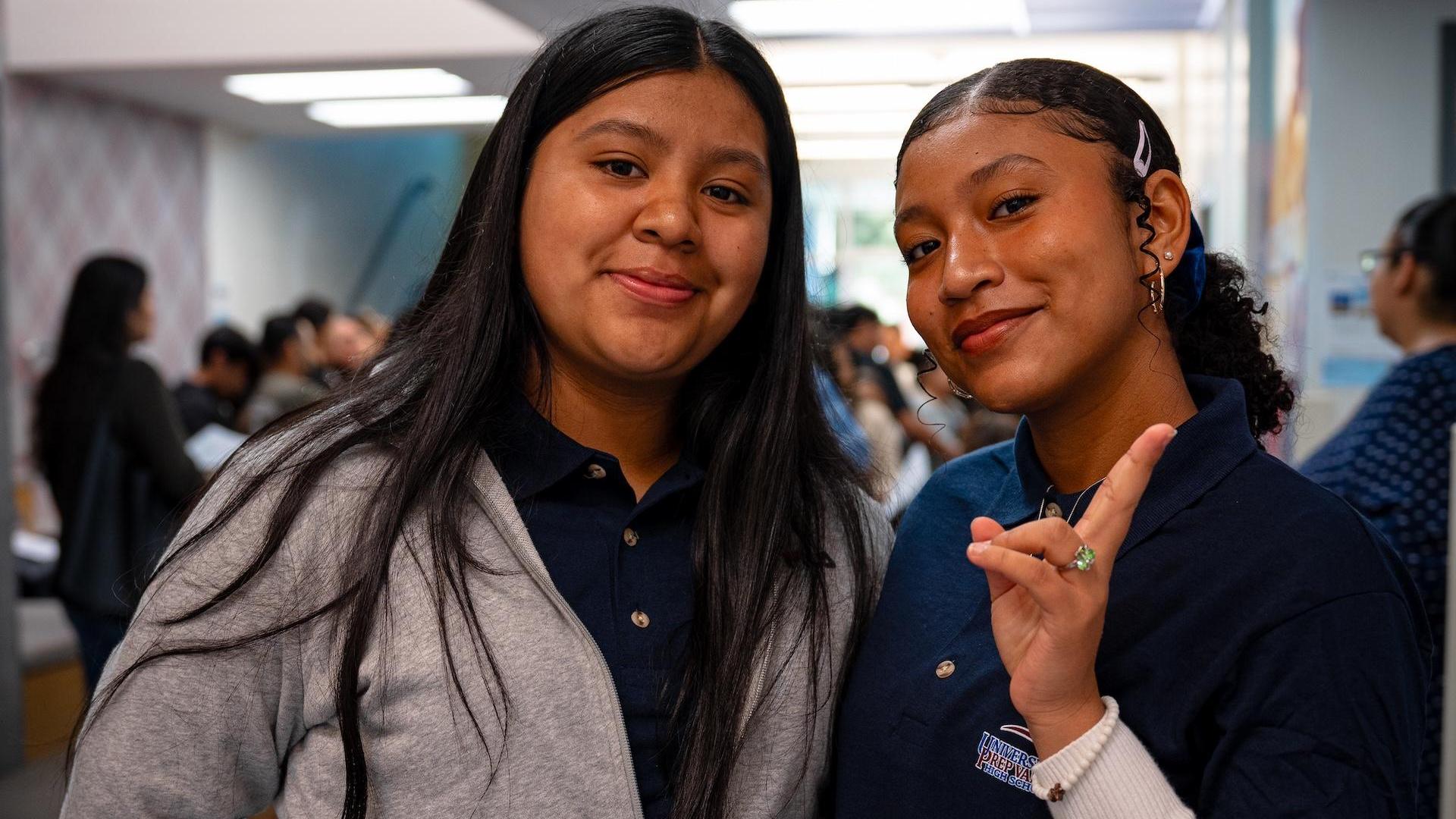 Two girls smile for the camera, one making a peace sign.