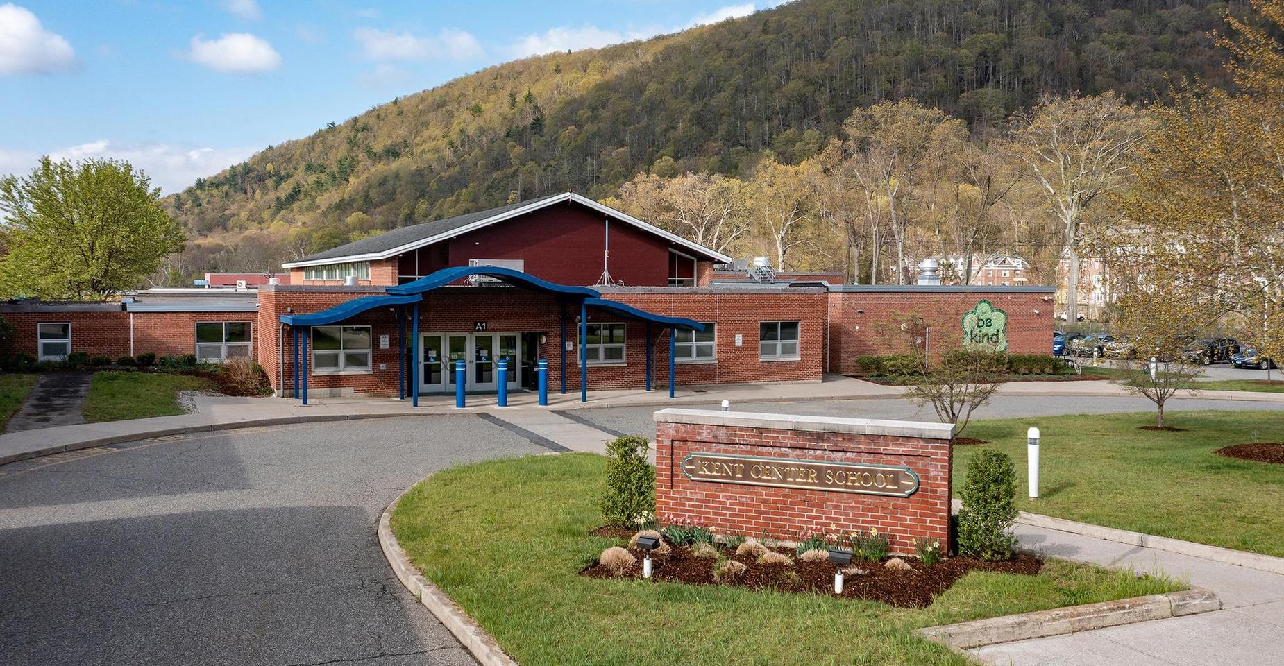 A brick school building with a landscaped entrance and a mountain backdrop.