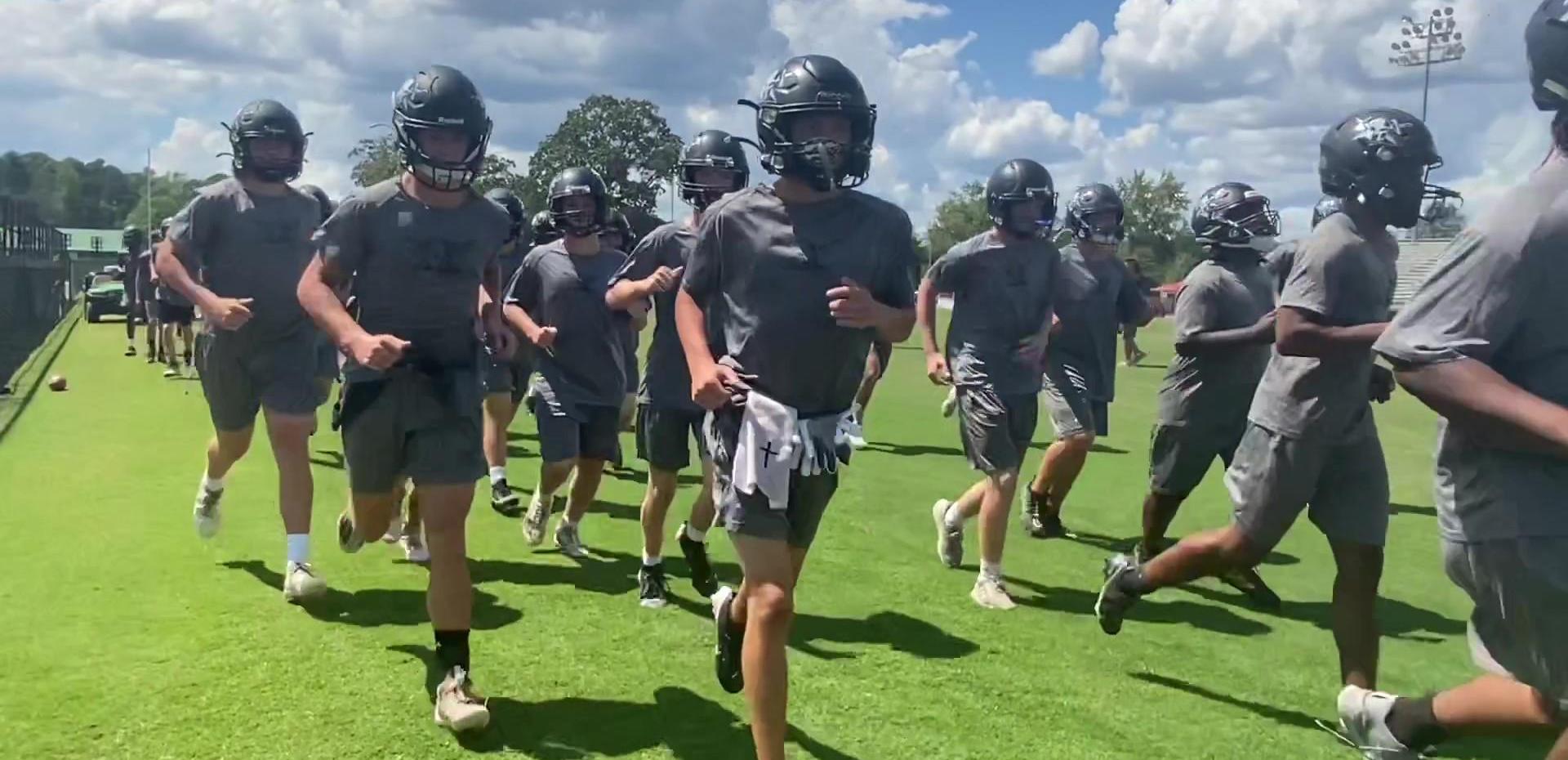 High school football team practicing on a sunny day.