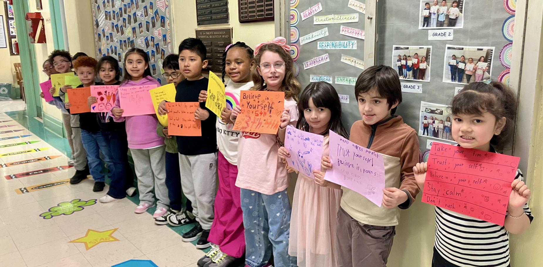 Group of children holding colorful signs with motivational messages in a school hallway.