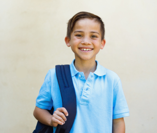 Elementary school boy wearing a backpack and smiling at the camera