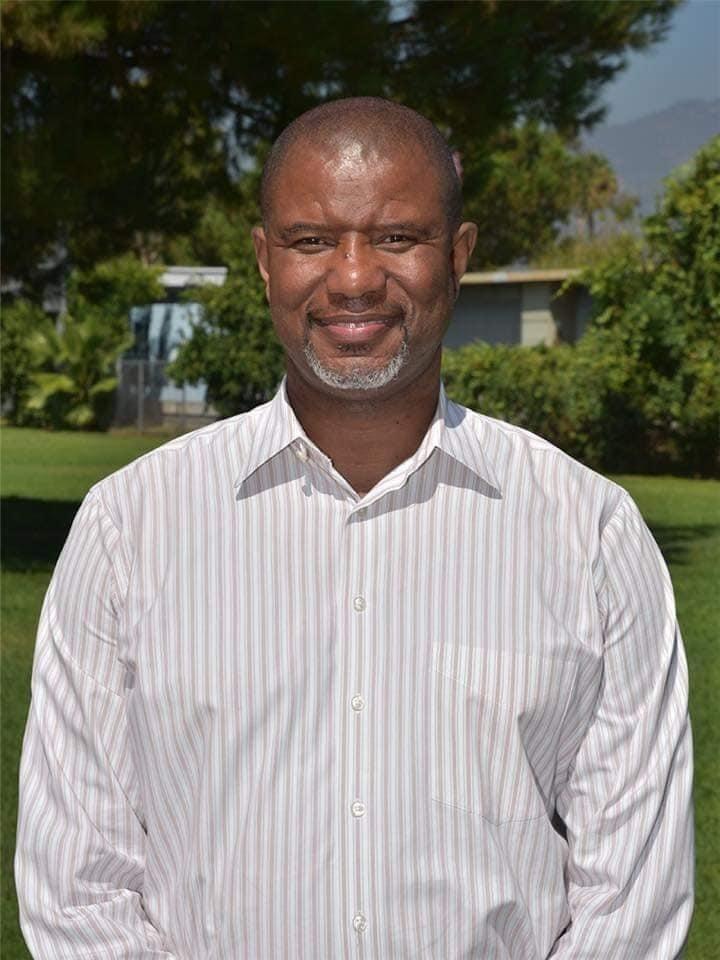 Kevin Morris, smiling in a striped shirt standing outdoors with greenery in the background.