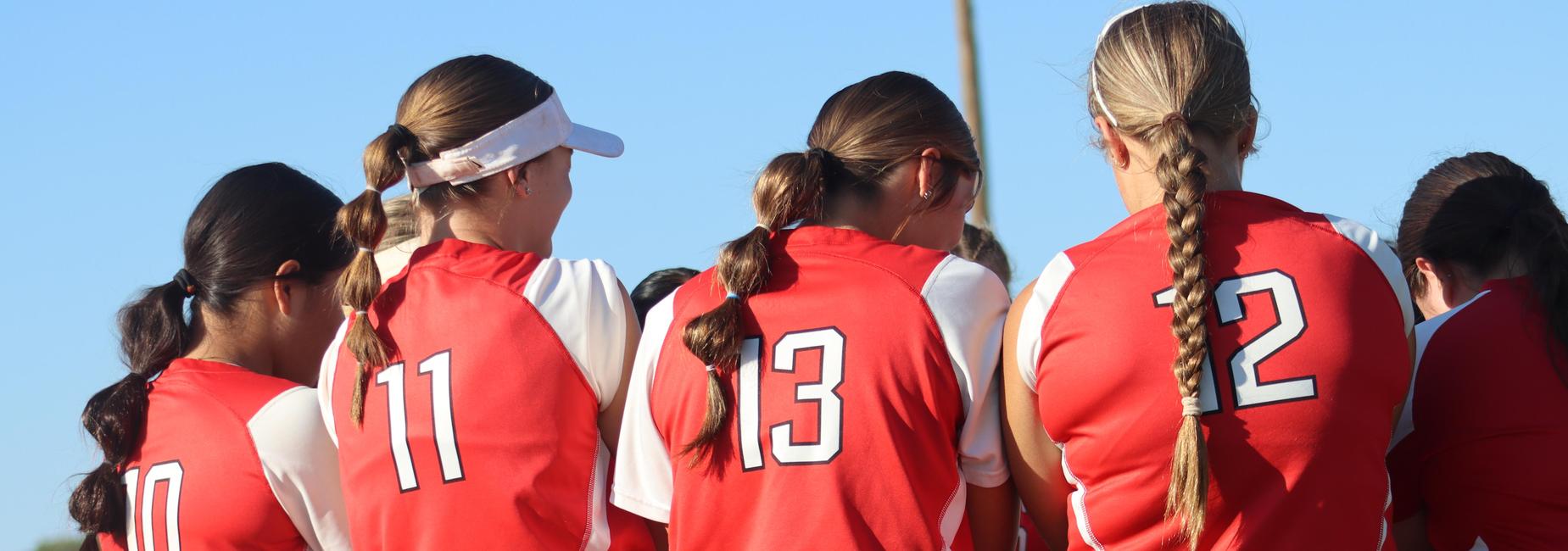 Players in red jerseys with their backs to the camera are sitting on a bench, focused.