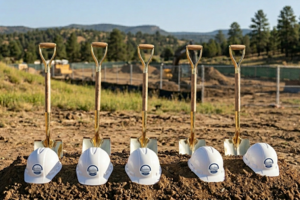 Ceremonial shovels stuck upright in a mount of dirt, behind white hard hats with the Durango School District logo