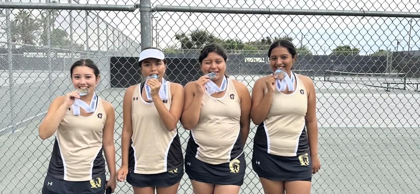 Four female tennis players holding medals, standing together by a fence.