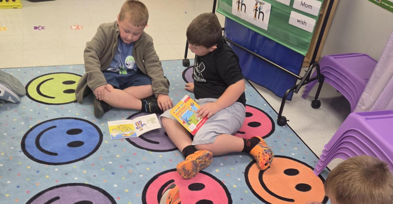 Three children reading books on a colorful smiley face carpet.