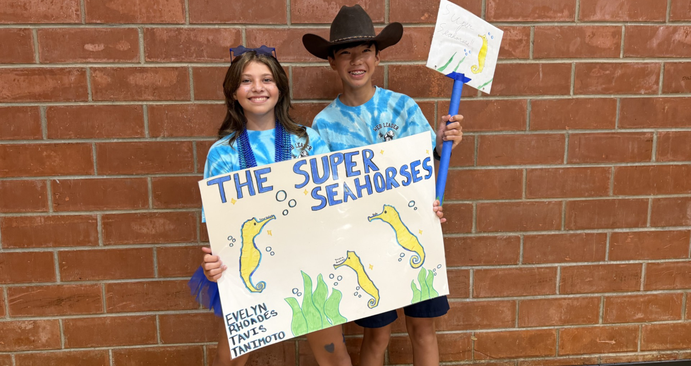 Two kids in blue shirts hold a sign that says 'The Super Seahorses' with drawings.