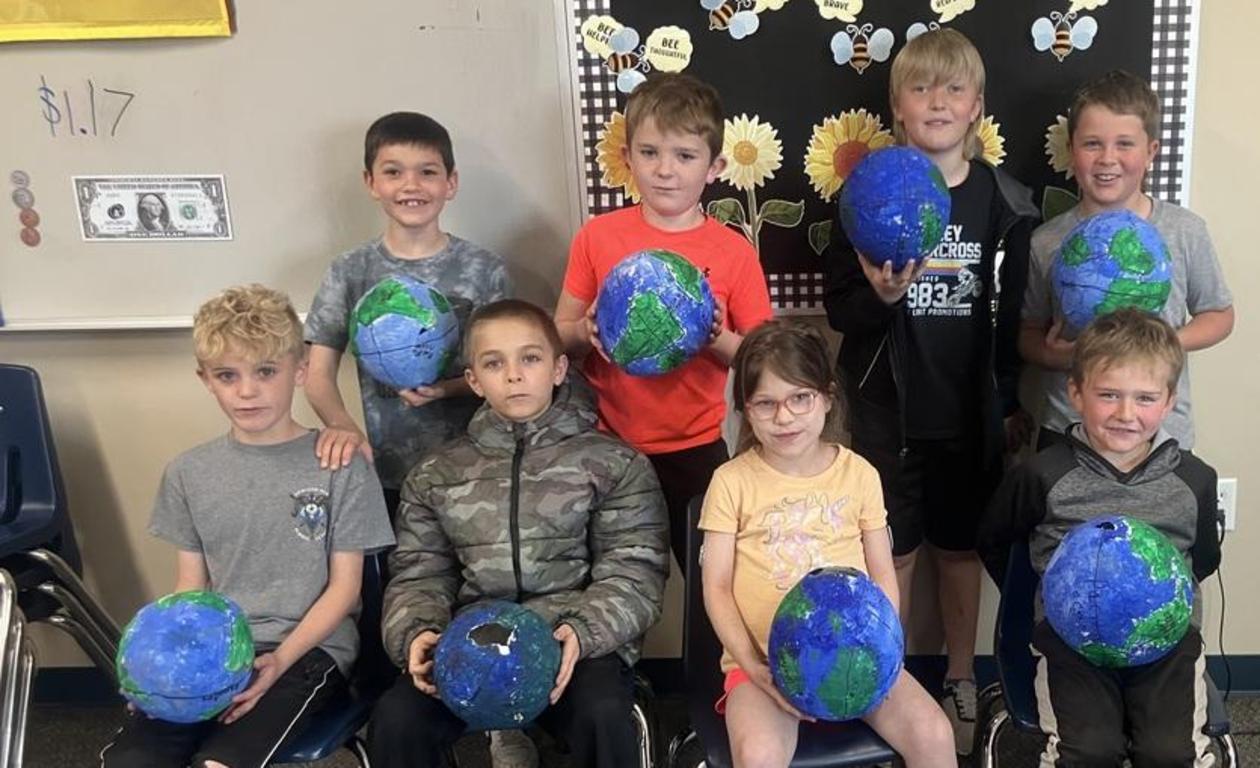 Eight kids sit together holding handmade globes, showcasing their art projects.