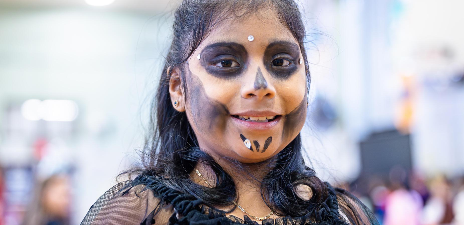 Child with skull makeup and a smile at a festive event.