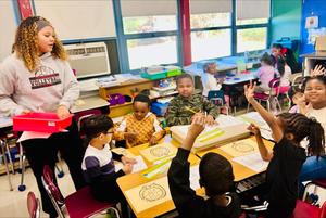 high school student stands next to table of elementary school students