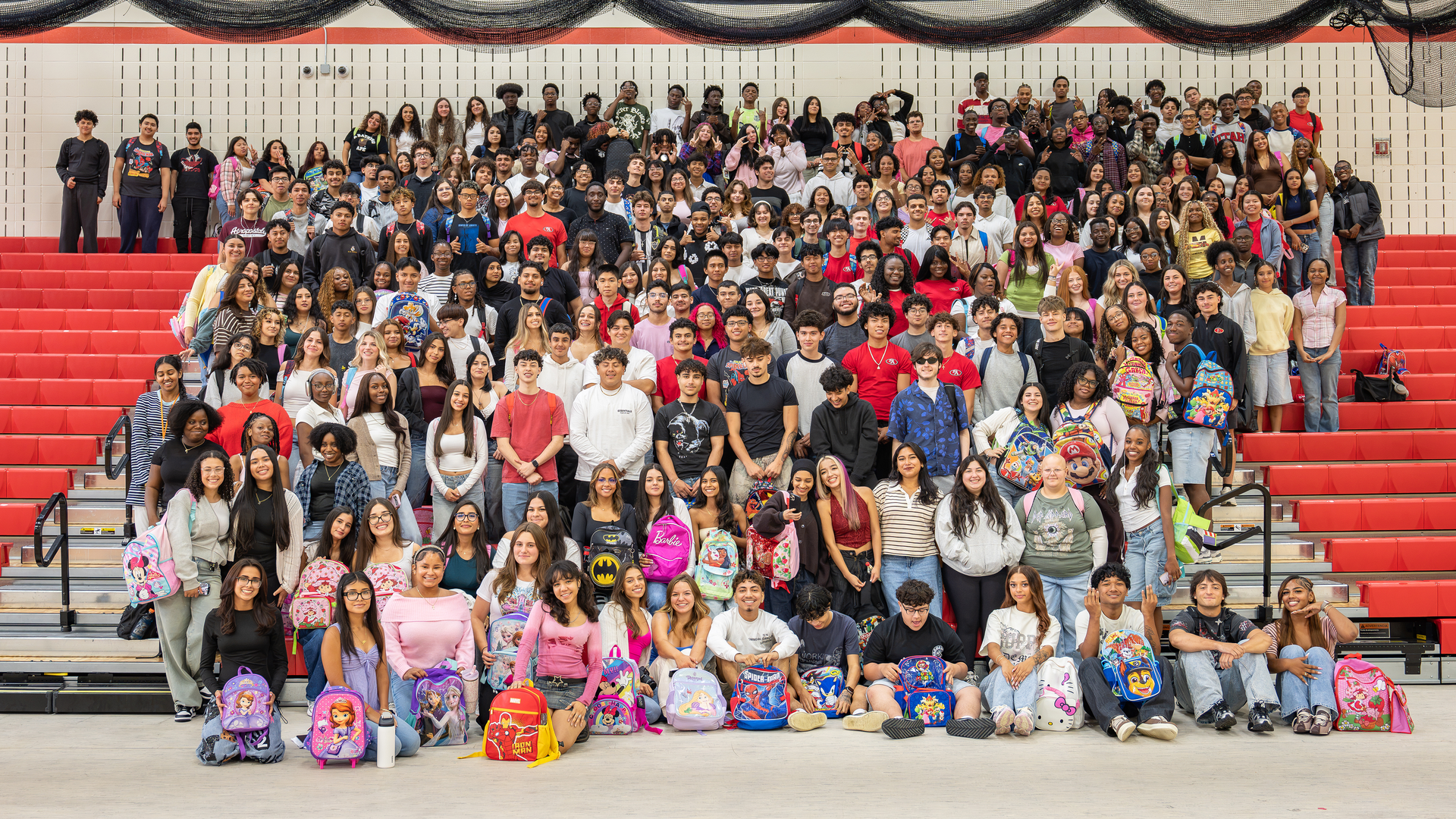 Group photo of a large crowd of students with backpacks in a school auditorium setting.