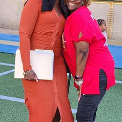 Two women smiling together, one in a rust-colored dress and the other in a red shirt.