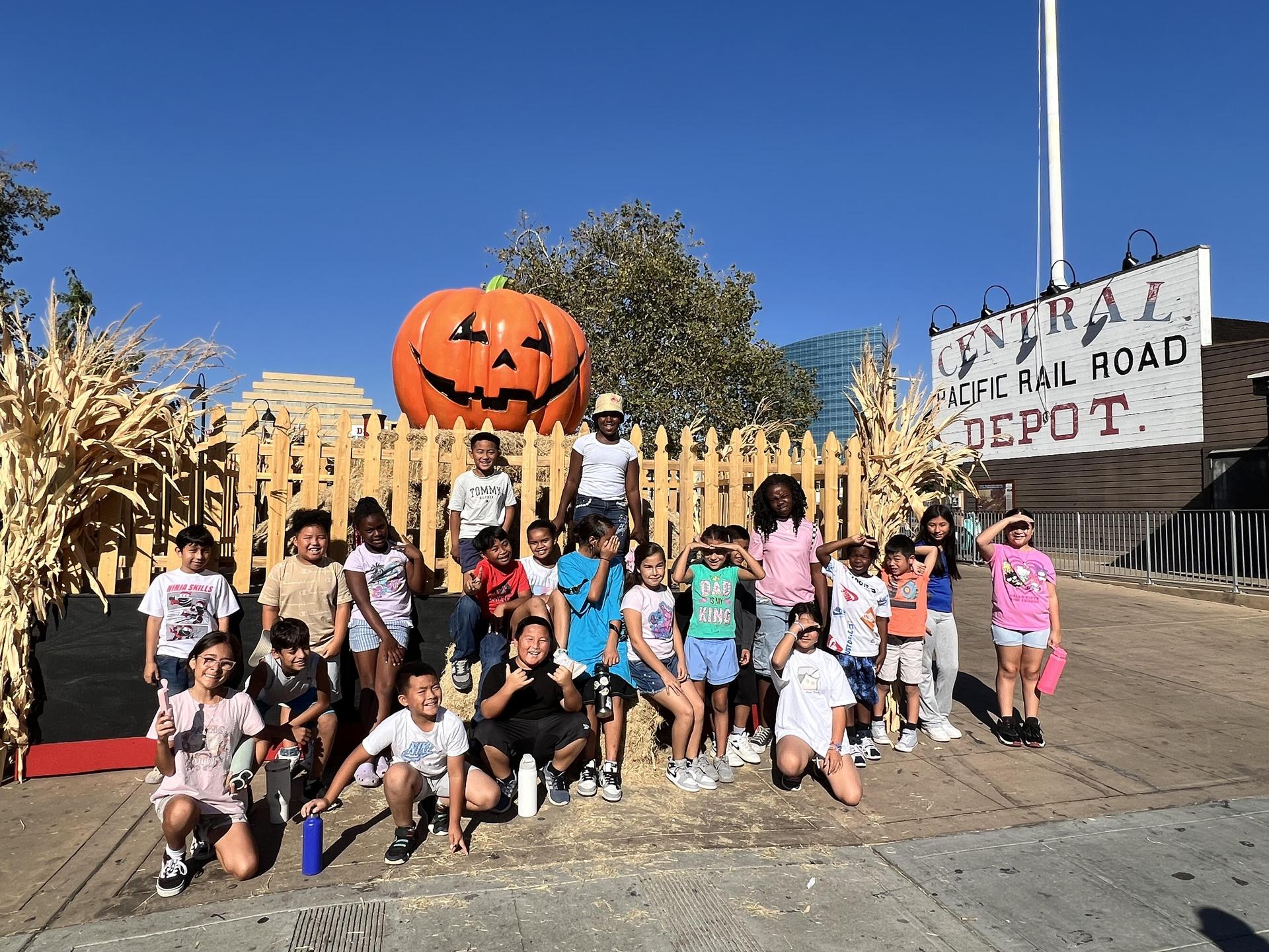 class posing for group photo in front of giant pumpkin